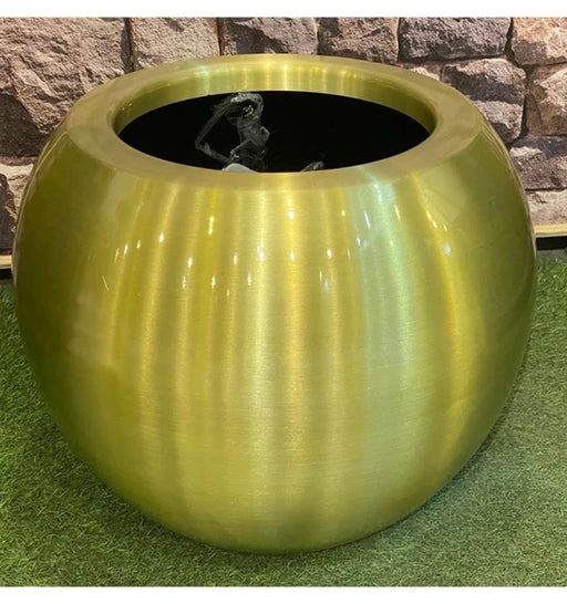 Green metallic planter with ribbed texture against a stone wall background