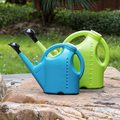 Two colorful watering cans, one blue and one green, on a stone surface with a garden background.