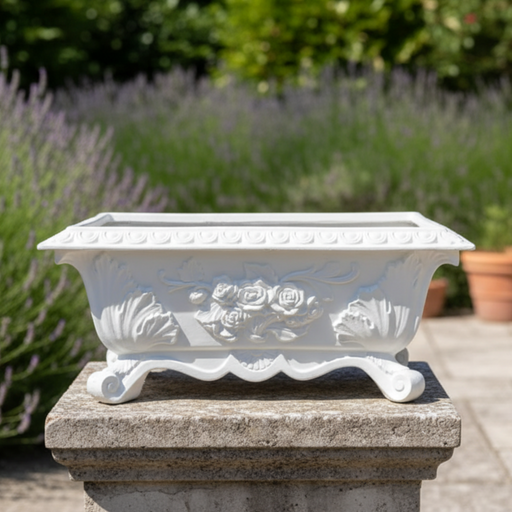 Decorative white planter with floral design on a stone pedestal against a garden background.