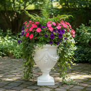 Decorative white urn planter with pink and purple flowers on a stone patio
