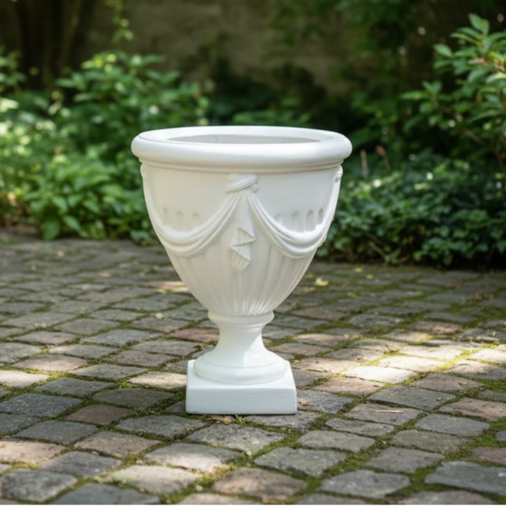 Decorative white urn on a stone patio with greenery in the background
