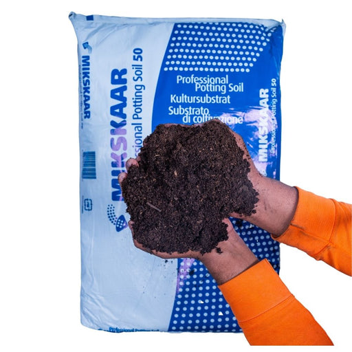Hand holding potting soil in front of a blue MIKSAAR bag